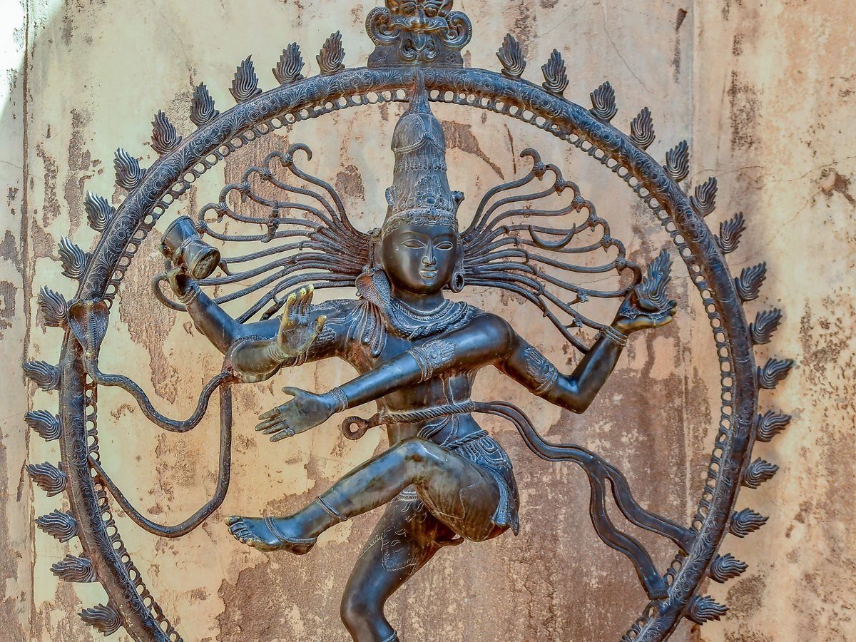 A bronze Shiva Nataraja, the dancing Shiva inside a ring of flame, against a weathered plaster wall