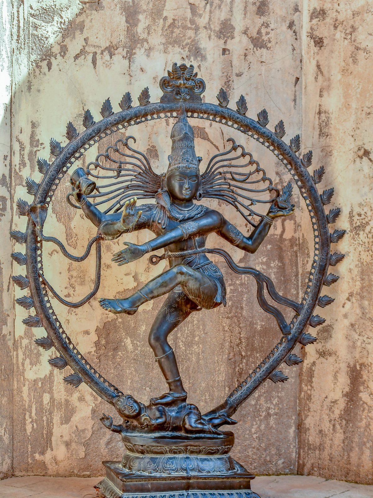 A bronze Shiva Nataraja, the dancing Shiva inside a ring of flame, against a weathered plaster wall