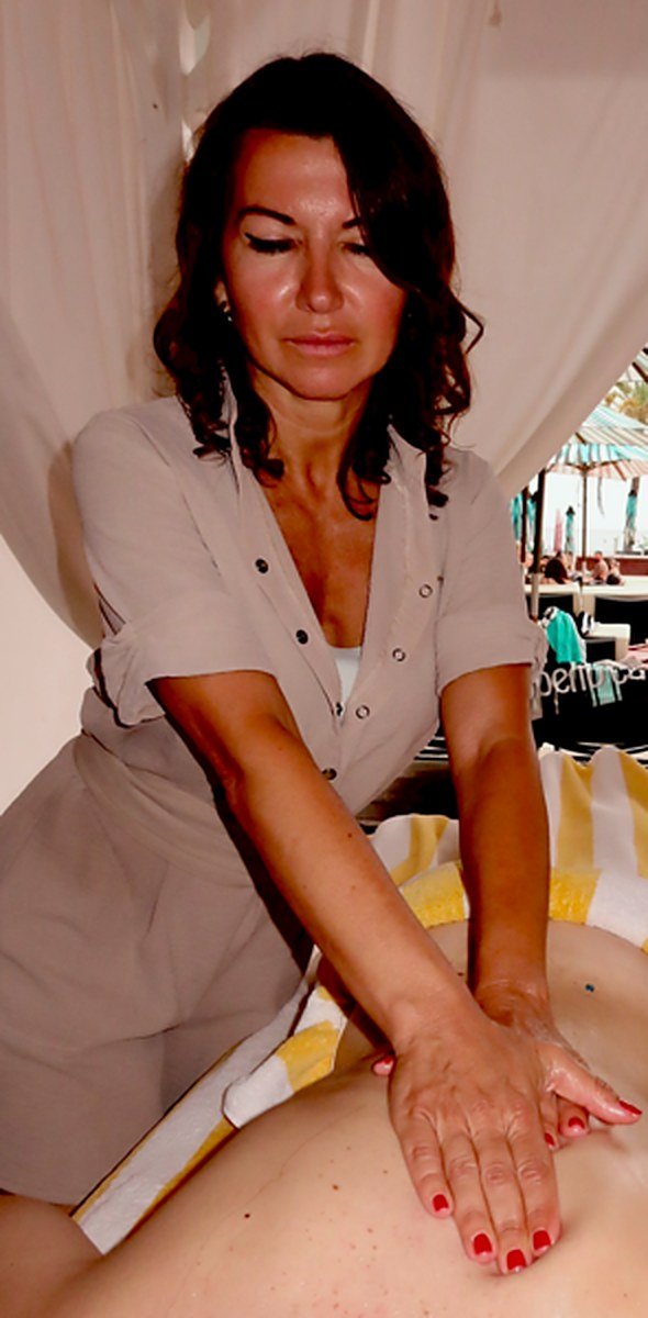 Jessica in a linen work dress giving a back massage in an open-air cabana, both hands on the client's lower back